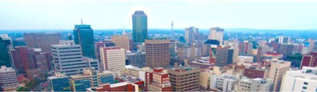 Over a lifetime, the Harare skyline has changed beyond recognition. With notable exceptions – the High Court, the foreign ministry, the Munhumatapa building ( time on the clock tower has long been stopped at twenty past three) - most of the squat colonial buildings are gone, giving way to gleaming towers of steel and glass.  An old man on his first trip from deep in the rural areas marvelled at the new buildings and remarked that us the townspeople appeared to be obsessed with glass. “You even cover your eyes with it,’’ he said to a bespectacled me.  He wasn’t impressed at all by the Karigamombe Centre or the faded gold façade of the Rainbow Towers – “Golden Delicious” as it was known to taxi drivers before the elements of sun and storm took their toll on the then Sheraton. Nor was he impressed by the imposing edifice of the central bank.  On the bus on the main road from the west he could see the Reserve Bank from some 20 kilometers away. It is designed to be seen from all the city’s main approach roads. He didn’t know until I told him that the bank’s octagonal design is symbolic of an upended maize cob - maize being the once abundant staple food and the cob-like skyscraper represents the Horn of Plenty, the nation’s cornucopia. Inside, it has marble trimmings and suites and boardrooms to match the best in Frankfurt or London. Alas, as the economy took strain in recent times, the Horn of Plenty emptied soon emptied.  A few blocks away, across my home town, is Eastgate, a fine shopping mall and office complex behind Meikles hotel that has rows of rooftop chimneys. When the building is lit after dusk it looks like an old steamship ploughing into the night. It was Zimbabwe’s first really “green” construction project, based on nature’s self-ventilating anthill. Its designers insisted it saved 70 percent of the energy costs the central bank building would gobble up.  Walking on chill winter mornings in the multiple green belts and vleis of Harare, I have often watched condensation stesteaming from the conical anthills as the worker ants aerated the depths of their nest.  Beautiful Harare is much like other former British colonial capitals whose planners allowed for plenty of tree-lined avenues and open spaces, quite unlike the cities in former French or Portuguese territories. Late in the year, we are washed with the magnificent lavender blossoms of the prolific jacaranda tree. The main square, Africa Unity Square, has been a sight to behold for as long as I can remember at jacaranda time.  The flower sellers and curio stalls add their colour to the square but the central fountains don’t seem to perform their kaleidoscopic water dance anymore. I wondered in the 1970s why they pulled down the fine old fashioned Meikles hotel, but it was progress, we were told. The old Meikles had a Palm Court orchestra in the ballroomplaying jazz standards and tea-room waltzes.  The square on Meikles’ north side was where the colonial era settlers raised the Union flag right opposite The Herald offices of today. They hadn’t intended to set Fort Salibury here, but it was unclear where a better site for the catchment of natural water was to be found. By the time it was, it was too late to move the settlement. So Harare is actually in the wrong place.  An underground water course runs along Seke Road and Julius Nyerere Way up to Harare Gardens and the Avenues district of apartments and townhouses. When I lived in the Avenues, my uncle, a water diviner, believed one reason I slept uneasily could be that my bed was placed east-to-west, against the flow of the water beneath. I was in its negative field. I moved the bed north-to-south. It worked. But it might have been a psychological thing, I suppose.  Back then, the dormitory township of Chitungwiza was mushrooming 25 kilometres to the south of the city centre and it was proposed by various armchair engineers that the underground river could be excavated and made into a canal for commuter barges. We could become the Venice of Africa…The idea, of course, never got beyond the armchairs.  In any city, there is always a dividing line between the ritzy executive offices and the hugger mugger of real life. Ours is Julius Nyerere Way. Cross it going west and enter a bustling tumult of wholesalers, shoe shops, stores for cheap clothing, haberdashery and aromatic spices, cafés, take-aways and liquor marts blaring loud Afro-pop over the pavement. And beyond that, of course, there are the “high density” suburbs, once the segregated townships where colonial planners put the workers needed for Harare’s factories and businesses.  Harare’s political nationalism has its mother lode in Highfield township where as young reporters many, many moons ago, we enjoyed the bars, shebeens and hotels – notably the Mushandire Pamwe hotel _ and listened to real township music at the Saratoga nightclub.  My own “low density” suburb of Eastlea awakens with the surround-sound of the dawn chorus that no iPod could ever match. An artist friend of mine advises the best way to start the day is to listen to the birds for five minutes before switching on news programmes or beginning other stressful activities. The dawn chorus today may be accompanied by the rumble of petrol generators.  I regard Harare, even though it’s worn, littered and horrifically potholed right now as my town and I love it. I and journalist colleagues of my vintage knew almost all the nationalists after whom streets were renamed after independence. In my travels over the years, I met Jason Moyo and Herbert Chitepo, both later to be murdered, and after 1980 I lived in a flat on Herbert Chitepo Avenue.   I had met Josiah Tongogara, I had befriended George “TG” Silundika, I knew Josiah Chinamano and I had spoken with or interviewed Nelson Mandela, Julius Nyerere, Kenneth Kaunda, Samora Machel, Sam Nujoma and – it should go without saying - President Mugabe.  The museum at Heroes Acre displays the old VW beetle in which a bomb killed Herbert Chitepo. We as reporters had dealings with almost all the fallen who lie at Heroes Acre. What’s more, if you have lived as a journalist in a city as long as I have there’s hardly a block of flats or an office building I haven’t been inside at some time or another, nor a bar, school, hospital, church, courthouse or even jail. You can’t say that about many capital cities of the world.  That’s where my father’s remains rest, there are the offices where the corporate vipers lied to us, that’s where my pension evaporated in hyperinflation, that’s where we held the wake for dear but tormented Frank Moore, a school friend, after his suicide 35 years ago. That’s the cemetery where Frank’s bones sleep, that’s where Catherine lived … reminding me whenever I pass it of John Le Carre’s words: there were some women who carried their bodies as if they were citadels to be stormed by only the bravest.  Maybe it’s a small town thing. Indeed, we are comparatively small and my Harare roots may well be comparatively shallow. But my dictionary defines: Roots, pl, n, the close ties one has with some place or people as through birth, upbringing, long association etc. I don’t care what anyone says. Harare, my birthplace, is home and, God willing, I’m not going anywhere else.