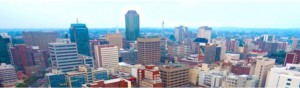 Over a lifetime, the Harare skyline has changed beyond recognition. With notable exceptions – the High Court, the foreign ministry, the Munhumatapa building ( time on the clock tower has long been stopped at twenty past three) - most of the squat colonial buildings are gone, giving way to gleaming towers of steel and glass. An old man on his first trip from deep in the rural areas marvelled at the new buildings and remarked that us the townspeople appeared to be obsessed with glass. “You even cover your eyes with it,’’ he said to a bespectacled me. He wasn’t impressed at all by the Karigamombe Centre or the faded gold façade of the Rainbow Towers – “Golden Delicious” as it was known to taxi drivers before the elements of sun and storm took their toll on the then Sheraton. Nor was he impressed by the imposing edifice of the central bank. On the bus on the main road from the west he could see the Reserve Bank from some 20 kilometers away. It is designed to be seen from all the city’s main approach roads. He didn’t know until I told him that the bank’s octagonal design is symbolic of an upended maize cob - maize being the once abundant staple food and the cob-like skyscraper represents the Horn of Plenty, the nation’s cornucopia. Inside, it has marble trimmings and suites and boardrooms to match the best in Frankfurt or London. Alas, as the economy took strain in recent times, the Horn of Plenty emptied soon emptied. A few blocks away, across my home town, is Eastgate, a fine shopping mall and office complex behind Meikles hotel that has rows of rooftop chimneys. When the building is lit after dusk it looks like an old steamship ploughing into the night. It was Zimbabwe’s first really “green” construction project, based on nature’s self-ventilating anthill. Its designers insisted it saved 70 percent of the energy costs the central bank building would gobble up. Walking on chill winter mornings in the multiple green belts and vleis of Harare, I have often watched condensation stesteaming from the conical anthills as the worker ants aerated the depths of their nest. Beautiful Harare is much like other former British colonial capitals whose planners allowed for plenty of tree-lined avenues and open spaces, quite unlike the cities in former French or Portuguese territories. Late in the year, we are washed with the magnificent lavender blossoms of the prolific jacaranda tree. The main square, Africa Unity Square, has been a sight to behold for as long as I can remember at jacaranda time. The flower sellers and curio stalls add their colour to the square but the central fountains don’t seem to perform their kaleidoscopic water dance anymore. I wondered in the 1970s why they pulled down the fine old fashioned Meikles hotel, but it was progress, we were told. The old Meikles had a Palm Court orchestra in the ballroomplaying jazz standards and tea-room waltzes. The square on Meikles’ north side was where the colonial era settlers raised the Union flag right opposite The Herald offices of today. They hadn’t intended to set Fort Salibury here, but it was unclear where a better site for the catchment of natural water was to be found. By the time it was, it was too late to move the settlement. So Harare is actually in the wrong place. An underground water course runs along Seke Road and Julius Nyerere Way up to Harare Gardens and the Avenues district of apartments and townhouses. When I lived in the Avenues, my uncle, a water diviner, believed one reason I slept uneasily could be that my bed was placed east-to-west, against the flow of the water beneath. I was in its negative field. I moved the bed north-to-south. It worked. But it might have been a psychological thing, I suppose. Back then, the dormitory township of Chitungwiza was mushrooming 25 kilometres to the south of the city centre and it was proposed by various armchair engineers that the underground river could be excavated and made into a canal for commuter barges. We could become the Venice of Africa…The idea, of course, never got beyond the armchairs. In any city, there is always a dividing line between the ritzy executive offices and the hugger mugger of real life. Ours is Julius Nyerere Way. Cross it going west and enter a bustling tumult of wholesalers, shoe shops, stores for cheap clothing, haberdashery and aromatic spices, cafés, take-aways and liquor marts blaring loud Afro-pop over the pavement. And beyond that, of course, there are the “high density” suburbs, once the segregated townships where colonial planners put the workers needed for Harare’s factories and businesses. Harare’s political nationalism has its mother lode in Highfield township where as young reporters many, many moons ago, we enjoyed the bars, shebeens and hotels – notably the Mushandire Pamwe hotel _ and listened to real township music at the Saratoga nightclub. My own “low density” suburb of Eastlea awakens with the surround-sound of the dawn chorus that no iPod could ever match. An artist friend of mine advises the best way to start the day is to listen to the birds for five minutes before switching on news programmes or beginning other stressful activities. The dawn chorus today may be accompanied by the rumble of petrol generators. I regard Harare, even though it’s worn, littered and horrifically potholed right now as my town and I love it. I and journalist colleagues of my vintage knew almost all the nationalists after whom streets were renamed after independence. In my travels over the years, I met Jason Moyo and Herbert Chitepo, both later to be murdered, and after 1980 I lived in a flat on Herbert Chitepo Avenue. I had met Josiah Tongogara, I had befriended George “TG” Silundika, I knew Josiah Chinamano and I had spoken with or interviewed Nelson Mandela, Julius Nyerere, Kenneth Kaunda, Samora Machel, Sam Nujoma and – it should go without saying - President Mugabe. The museum at Heroes Acre displays the old VW beetle in which a bomb killed Herbert Chitepo. We as reporters had dealings with almost all the fallen who lie at Heroes Acre. What’s more, if you have lived as a journalist in a city as long as I have there’s hardly a block of flats or an office building I haven’t been inside at some time or another, nor a bar, school, hospital, church, courthouse or even jail. You can’t say that about many capital cities of the world. That’s where my father’s remains rest, there are the offices where the corporate vipers lied to us, that’s where my pension evaporated in hyperinflation, that’s where we held the wake for dear but tormented Frank Moore, a school friend, after his suicide 35 years ago. That’s the cemetery where Frank’s bones sleep, that’s where Catherine lived … reminding me whenever I pass it of John Le Carre’s words: there were some women who carried their bodies as if they were citadels to be stormed by only the bravest. Maybe it’s a small town thing. Indeed, we are comparatively small and my Harare roots may well be comparatively shallow. But my dictionary defines: Roots, pl, n, the close ties one has with some place or people as through birth, upbringing, long association etc. I don’t care what anyone says. Harare, my birthplace, is home and, God willing, I’m not going anywhere else.
